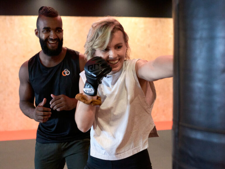 Un coach et une adhérente en plein cours de boxe dans une salle de sport L'Appart Fitness