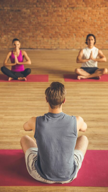 Un cours de Yoga à L'Appart Fitness avec un coach et deux participants pratiquant des postures de méditation dans une salle lumineuse et spacieuse.