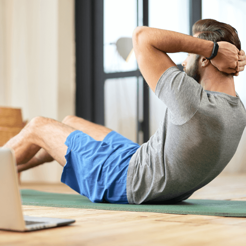 Un homme effectuant un exercice d'abdos sur un tapis de yoga à la maison, suivant un entraînement en ligne.